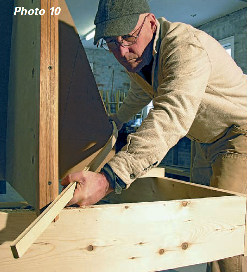 Man wearing glasses checks the bevel on a boat frame with a piece of planking stock