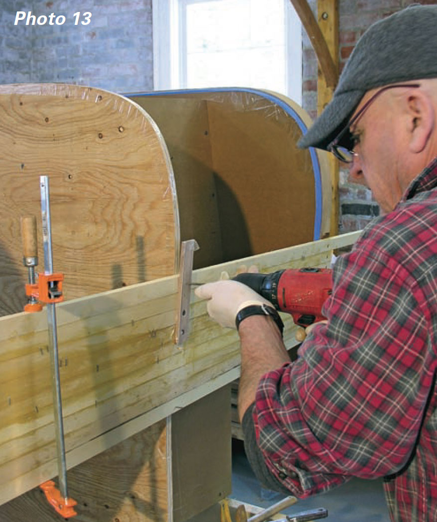 Man uses power drill to screw planks to a boat mold through a short strip of plywood.