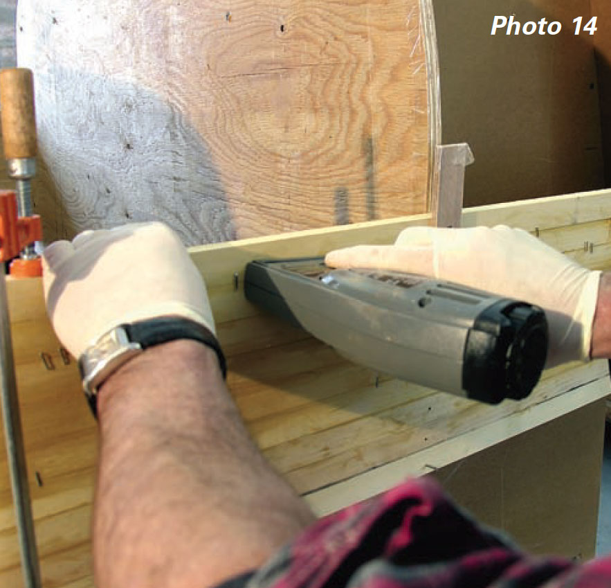 Hands holding an electric staple gun along boat planks.