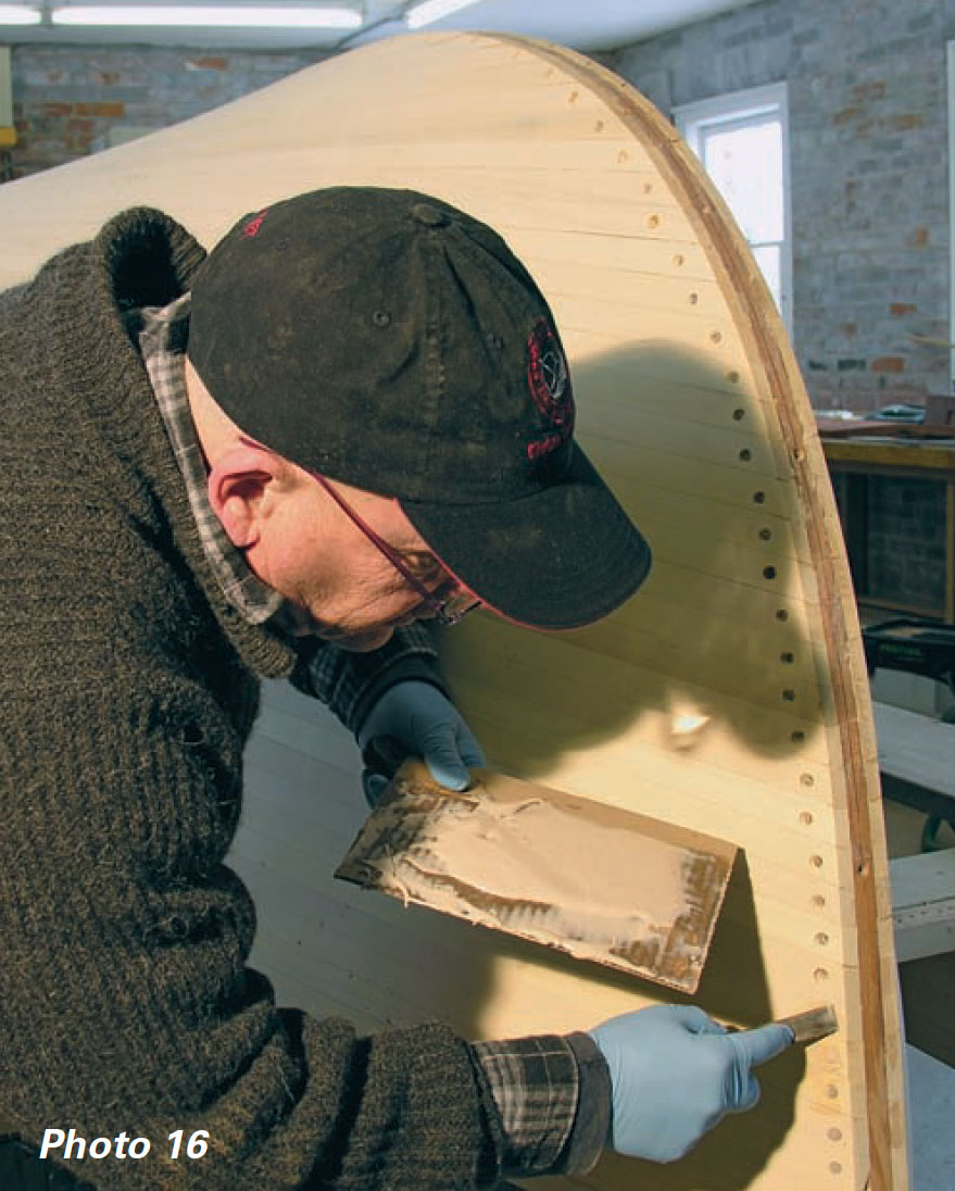 Man holds palette and applies thickened epoxy to screw holes and cracks between boat planks.