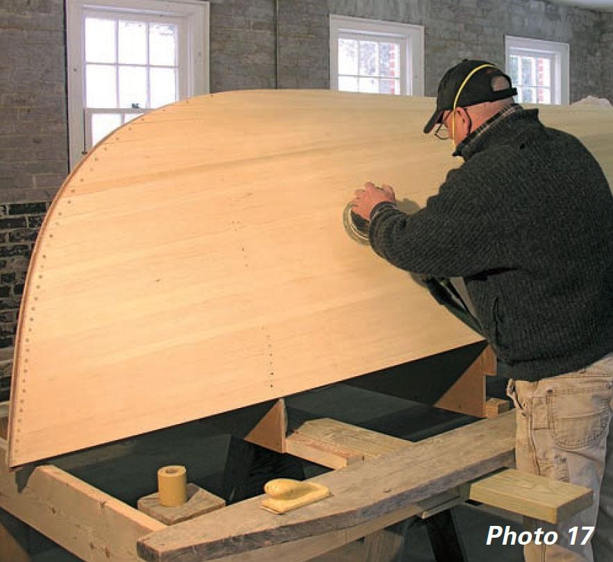 Boatbuilder uses orbit sander on boat hull.