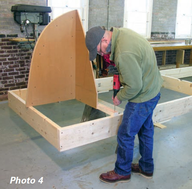 Boatbuilder fastens a wooden mold to a strongback frame using a power drill.