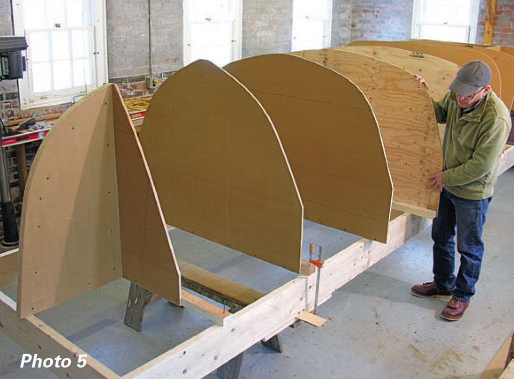 Man stands next to boat frame and adds final mold piece.