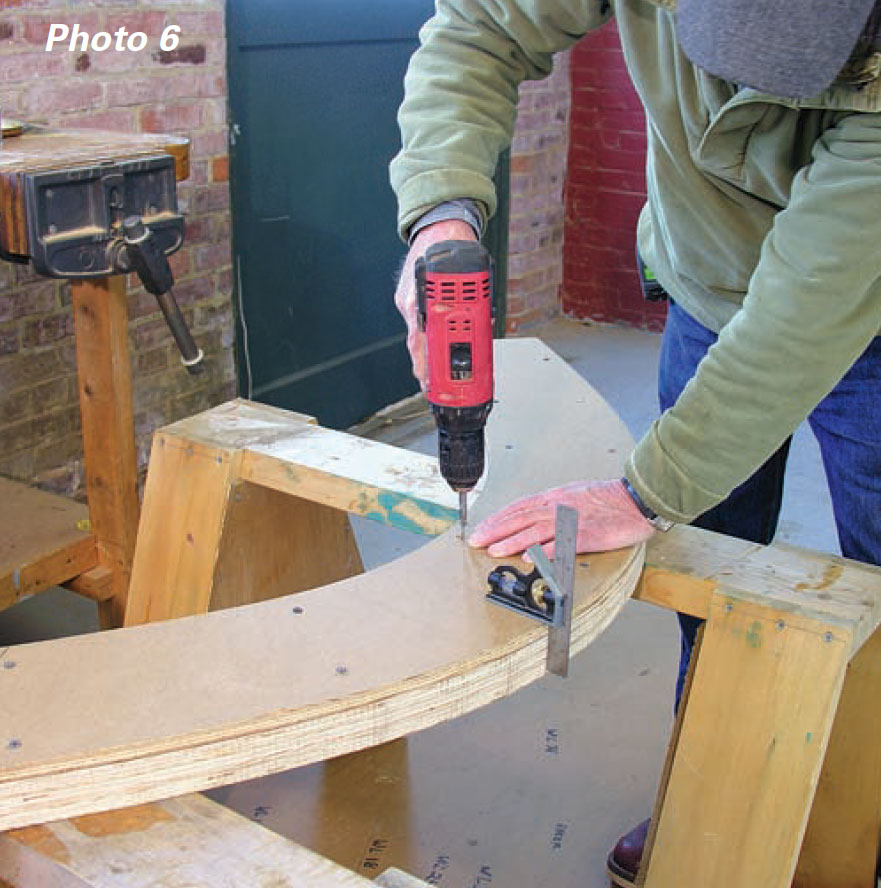 Man uses a power drill to attach a half-inch piece of plywood to part of a boat's stem.