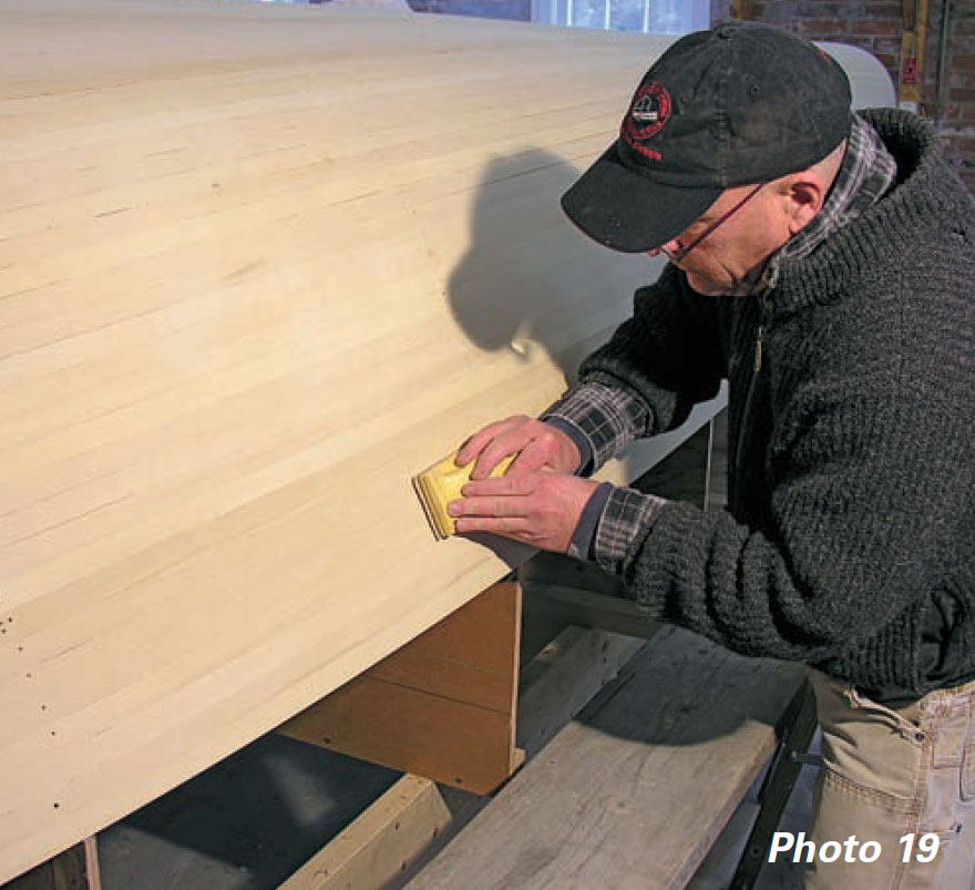 Man uses yellow foam sanding blocks to sand a boat hull fore and aft.