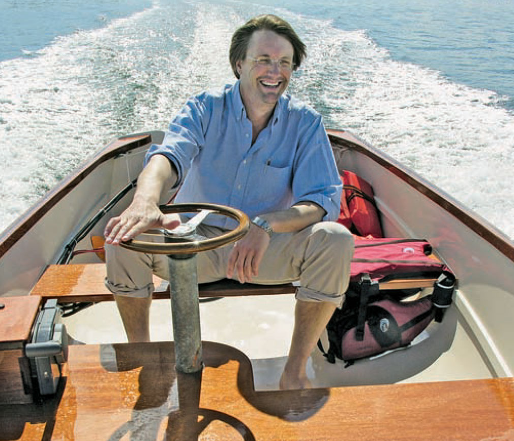 Smiling man in blue shirt steers powerboat while on the water.