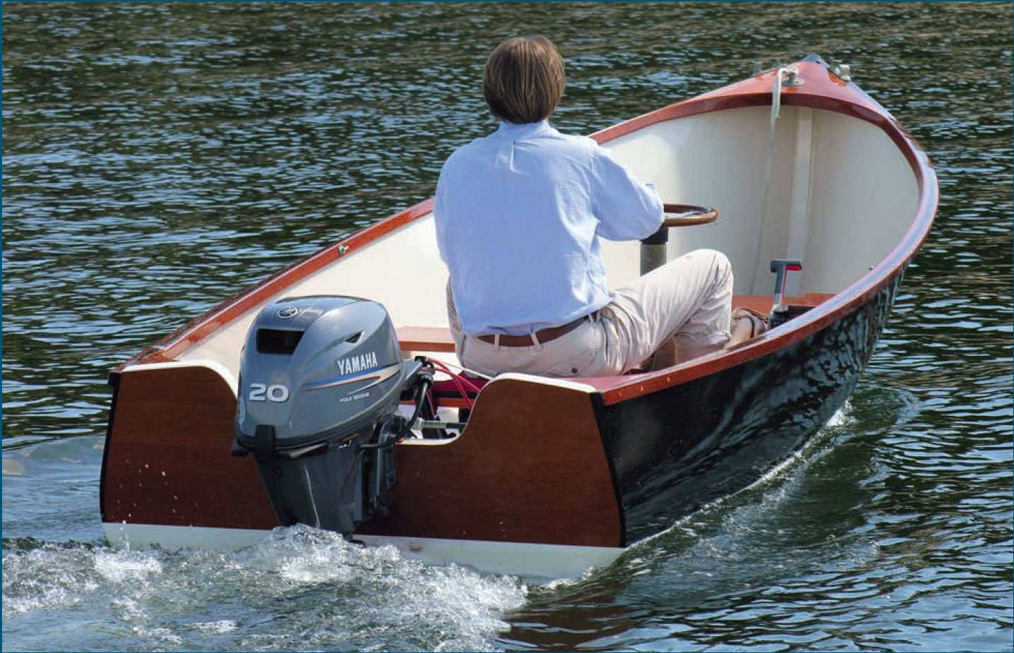 Man in blue shirt pilots motorboat with Yamaha outboard motor.