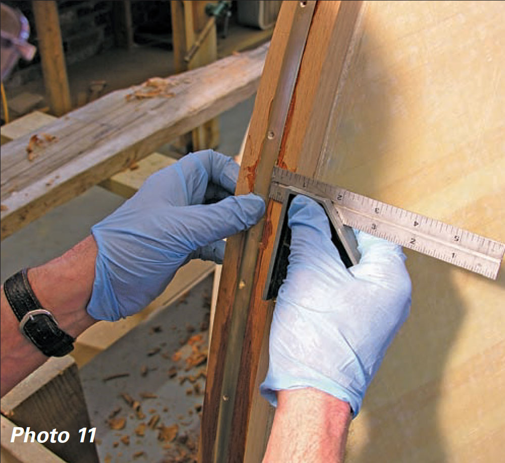 Gloved hands hold a combination square to a wooden boat stem.