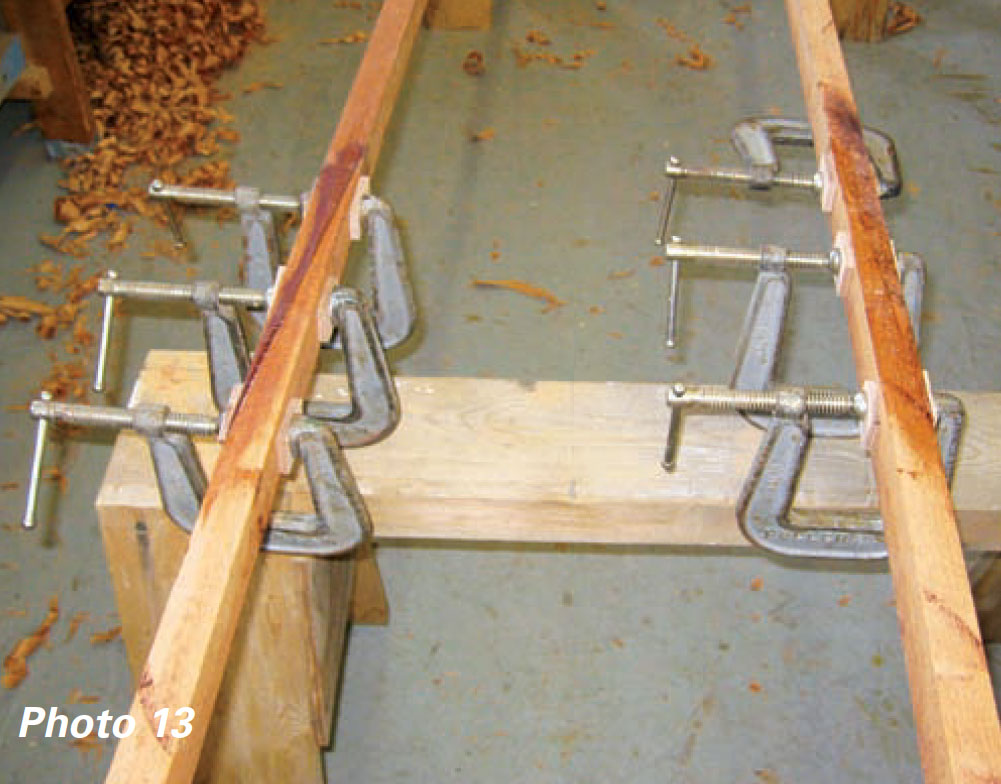 Six metal clamps hold glued wooden planks together.