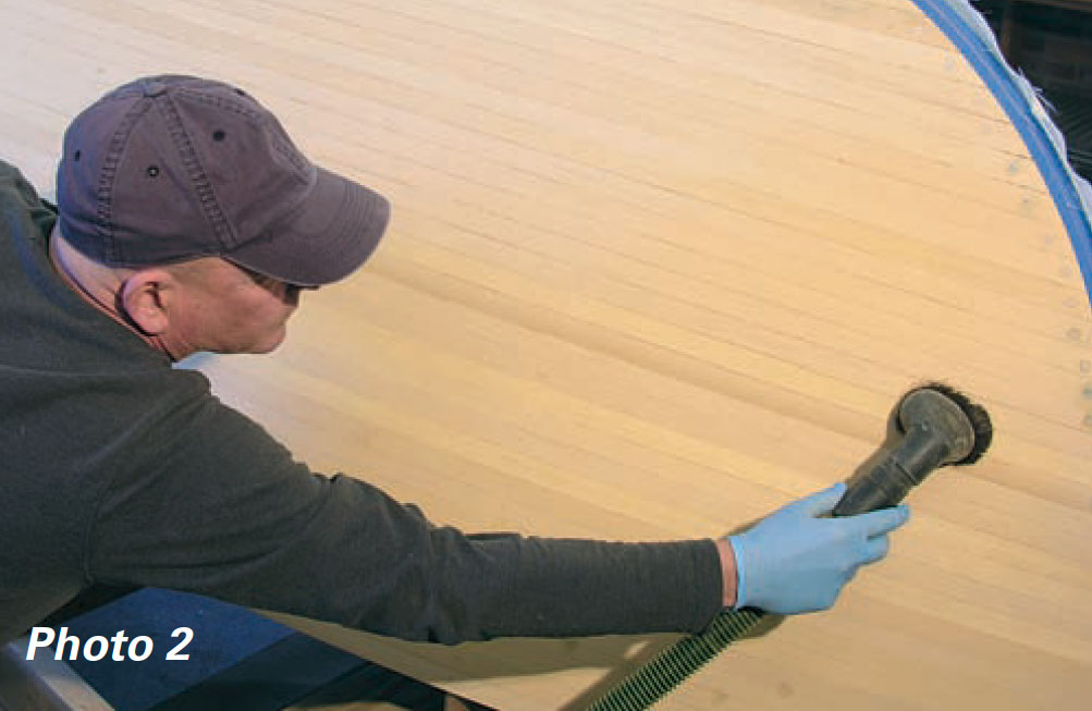 Man uses vacuum with brush attachment to clean a wooden boat hull.