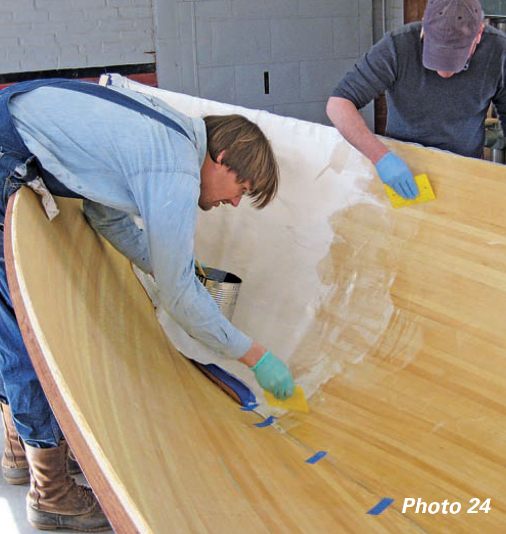 Two boatbuilders apply epoxy to a boat's inner hull.