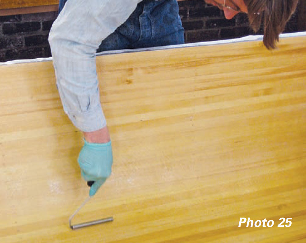 Man uses a rolling bubble buster to smooth fiberglass fabric on a boat's inner hull.