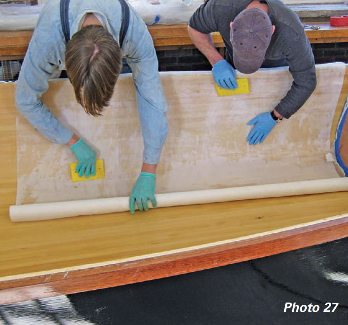 Two men use squeegees to smooth release fabric inside a boat's hull.