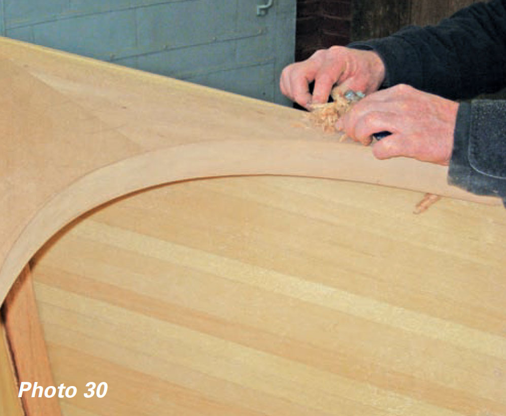 Hands use tool to shape a boat's breasthook.