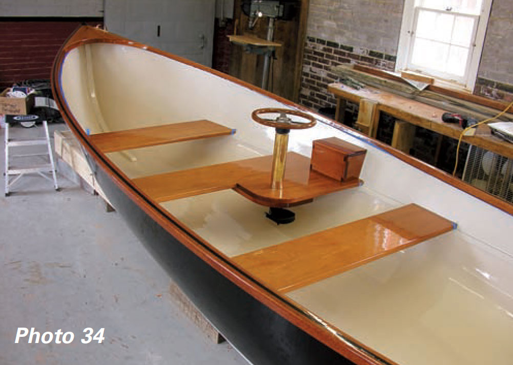 Three mahogany seats and a steering wheel inside of a nearly finished wooden boat.