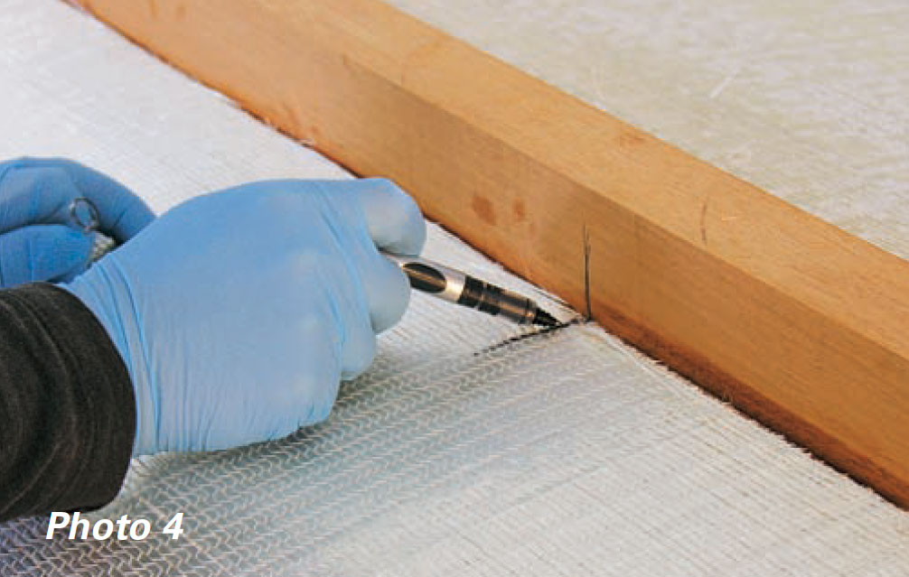 Two gloved hands mark a black line on fiberglass fabric with pen.