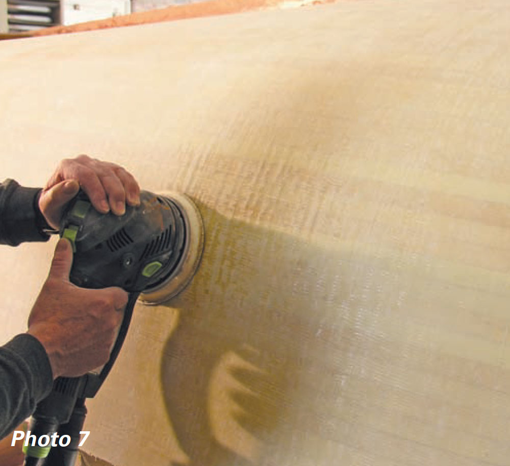 Hands holding an orbit sander to a boat hull.