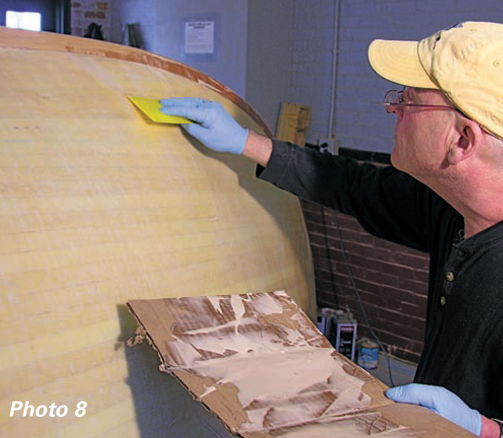 Man in yellow hat applies epoxy to a boat hull with a squeegee.