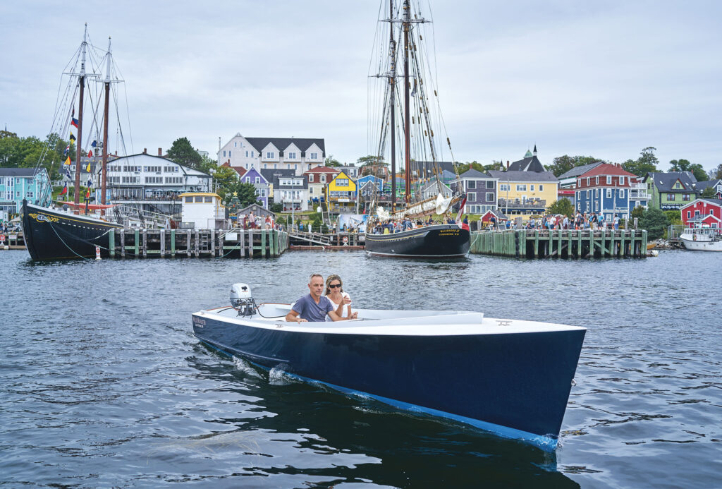 Man and woman riding in a blue powerboat with docked boats in the background.