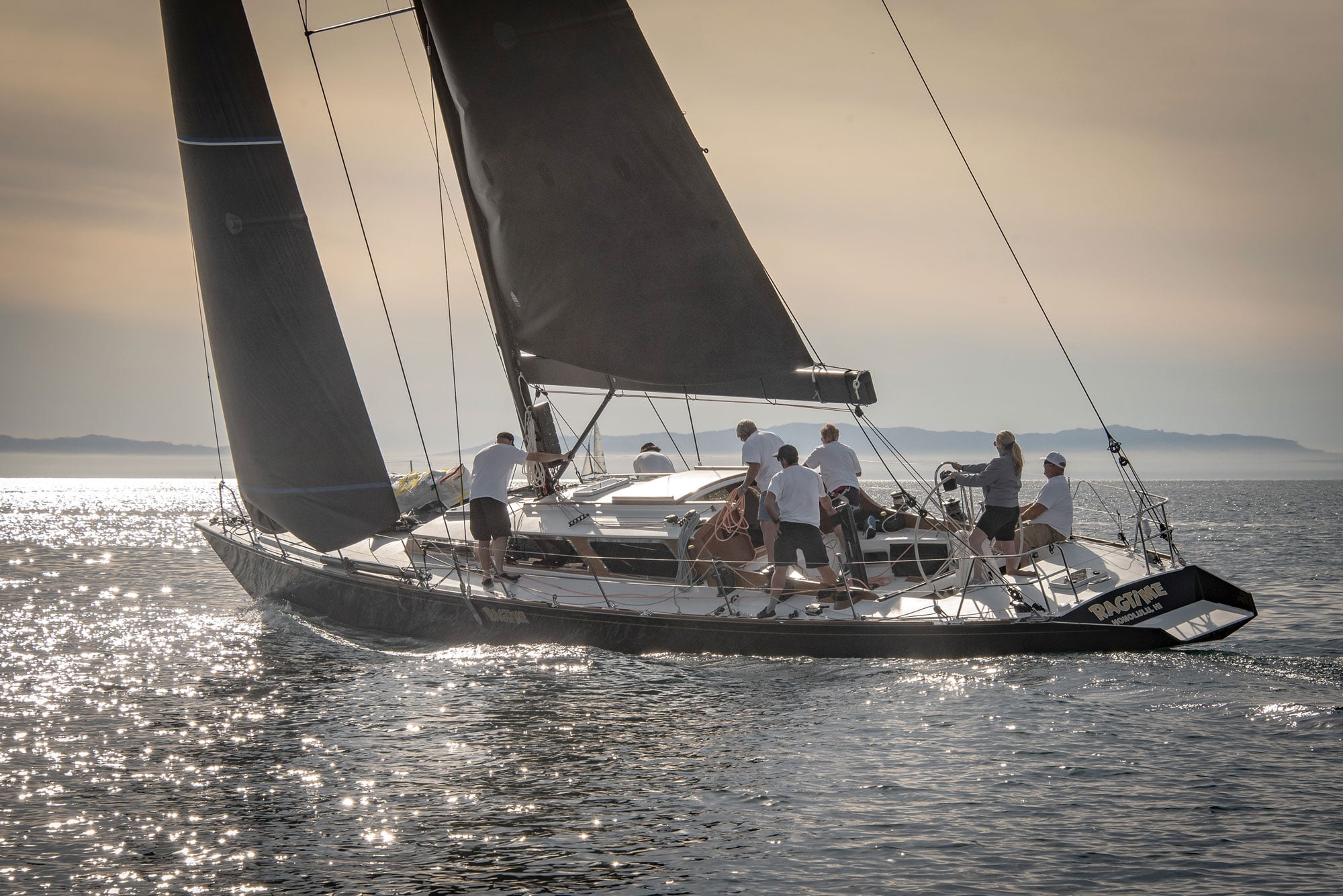 Sailors aboard RAGTIME as the sun sets and shines off the water.