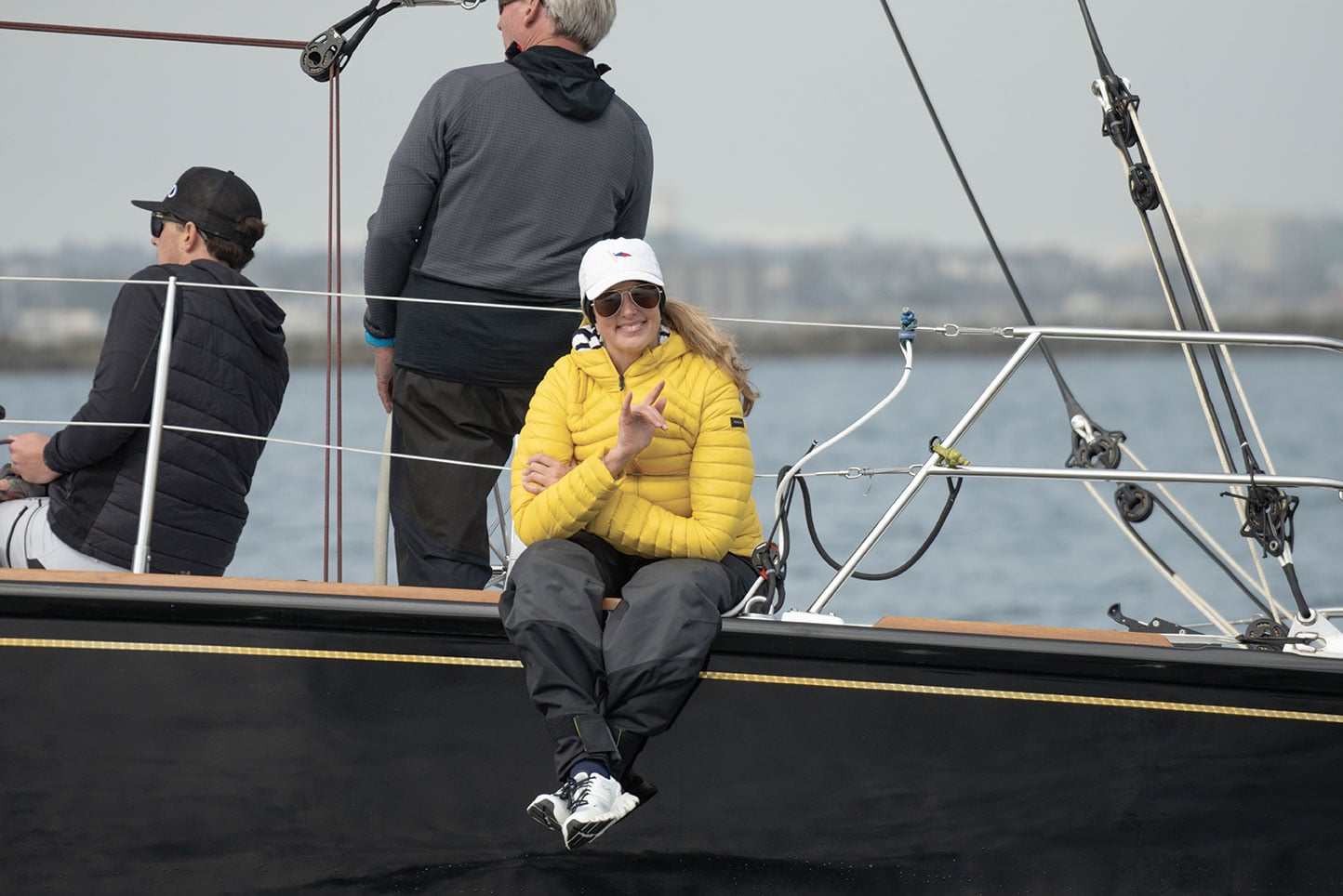 Woman in yellow jacket sits aboard the side of a wooden boat.
