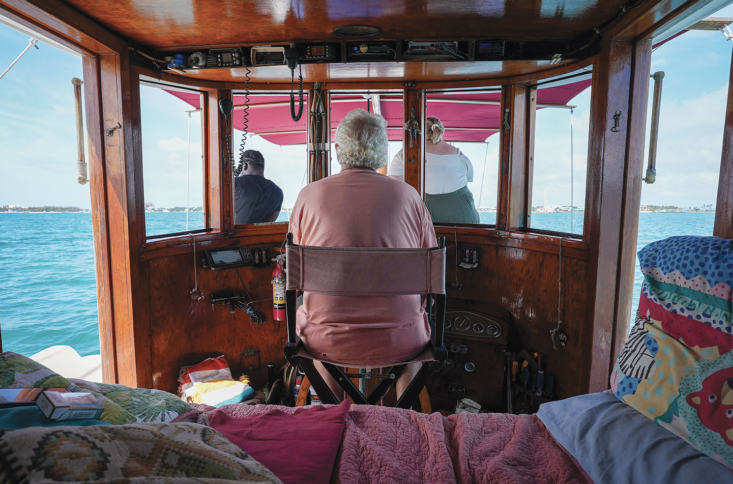 Man sits in a folding director's chair while piloting a wooden buyboat.