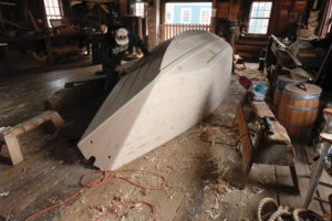 Boatbuilders working on a wooden-boat hull in a shop.
