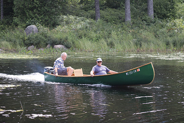 Two boaters pilot a green Grand Laker guide canoe with an outboard motor.